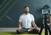 “거실이 곧 개인 훈련장”… AI 카메라와 홈트의 결합, ‘공간의 해방’ Man meditating on yoga mat recording with phone.